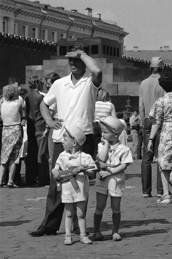 Двое маленьких мальчиков с игрушечными пулеметами в руках стоят с отцом на Красной площади среди толпы туристов со всего Советского Союза и мира. - Sputnik Беларусь