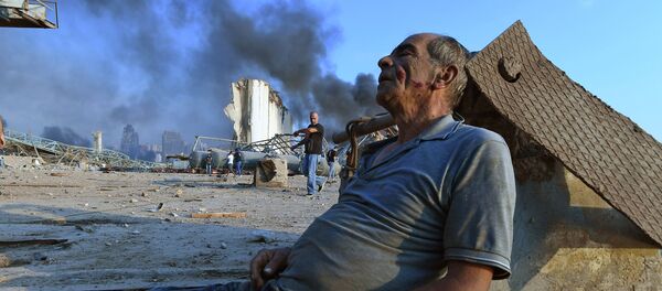 Пострадавший сидит на земле в ожидании помощи в порту Бейрута - Sputnik Беларусь