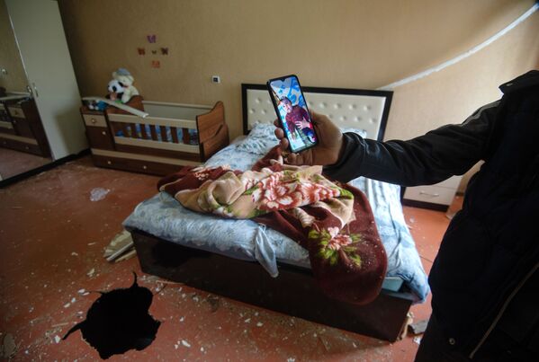 Мужчина показывает фотографию ребенка, который лежал в кроватке в момент попадания снаряда в дом - Sputnik Беларусь