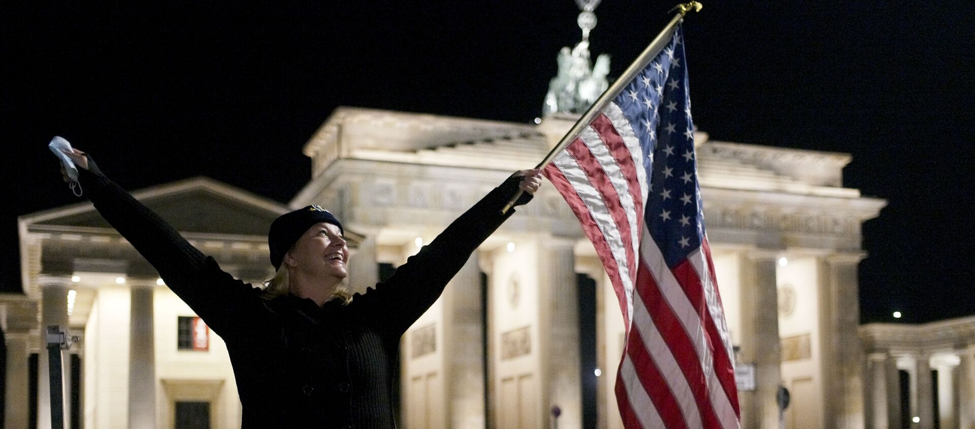 Женщина празднует победу Джо Байдена перед Бранденбагскими воротами рядом с посольством США в Берлине - Sputnik Беларусь, 1920, 13.11.2020