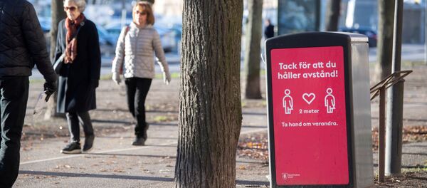 Люди в парке гуляют возле таблички с просьбой о соблюдении социального дистанцирования - Sputnik Беларусь