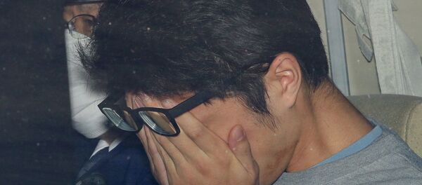 Такахиро Сираиси закрывает лицо в полицейской машине в Токио - Sputnik Беларусь