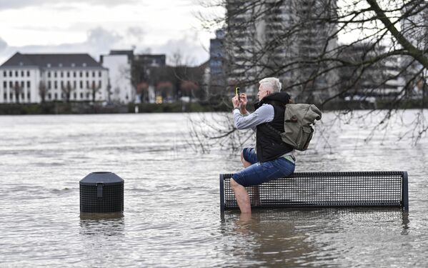 Мужчина делает снимок на свой смартфон, сидя на скамейке на затопленном берегу реки Рейн в Кельне - Sputnik Беларусь