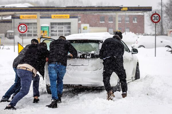 Водители выталкивают машину из снега, которая застряла на заправочной станции недалеко от Мюнстера, Германия - Sputnik Беларусь