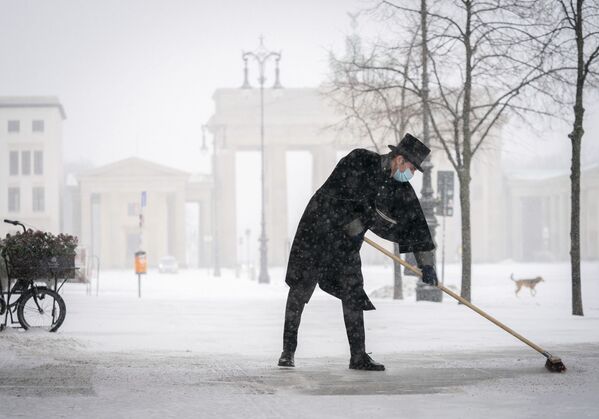 Сотрудник отеля Adlon очищает тротуар от снега на Парижской площади перед Брандебургскими воротами в Берлине - Sputnik Беларусь