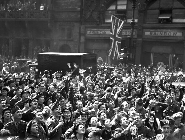 Британские граждане и военнослужащие союзнической армии собрались возле клуба американского Красного Креста на Рэйнбоу-коннэр недалеко от площади Пикадилли в Лондоне 7 мая 1945 года, чтобы услышать объявление о полной капитуляции Германии.  - Sputnik Беларусь