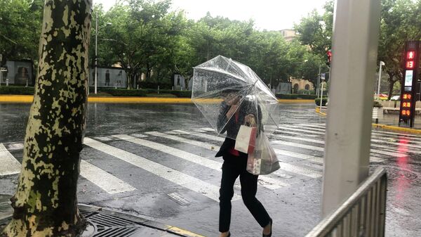 Женщина прячется под зонтиком от ветра и дождя в Шанхае в воскресенье, 25 июля - Sputnik Беларусь