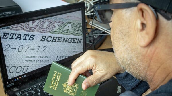 Мужчина из Марокко держит паспорт перед компьютером, на котором отображается шенгенская виза - Sputnik Беларусь