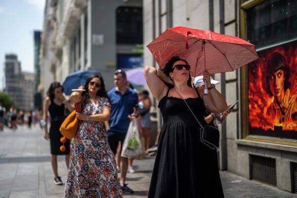 Женщина держит зонтик, чтобы укрыться от солнца в жаркий солнечный день в Мадриде, Испания. - Sputnik Беларусь
