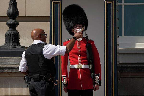 Полицейский поит британского солдата в традиционной медвежьей шапке, дежурящего у Букингемского дворца. - Sputnik Беларусь