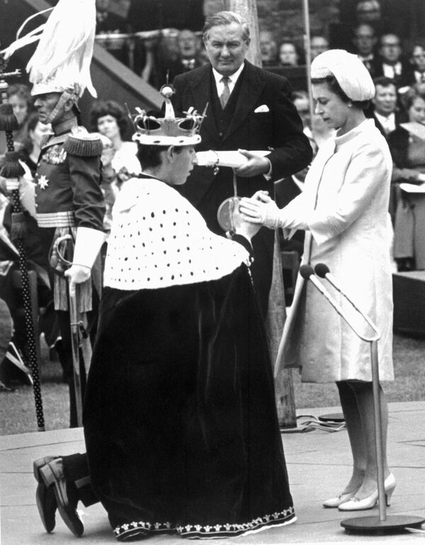 Британская королева Елизавета II держит за руки своего 20-летнего сына принца Чарльза во время присвоения ему титула принца Уэльского 11 июля 1969 года в замке Карнарвон, как того требует традиция. Теперь принцем Уэльским станет сын Чарльза, принц Уильям. Этот титул не передается автоматически. - Sputnik Беларусь