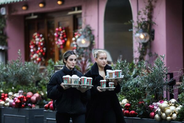 Две женщины несут напитки из Starbucks на празднично украшенной улице британской столицы. - Sputnik Беларусь