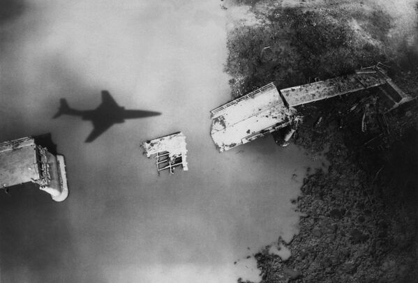 Сделанный в апреле 1965 года снимок американского разведывательного самолета Shadow of RF-101, пролетающего над мостом, разрушенным американскими обстрелами, в Северном Вьетнаме. Регулярные бомбардировки Северного Вьетнама США начали 2 марта 1965 года. - Sputnik Беларусь