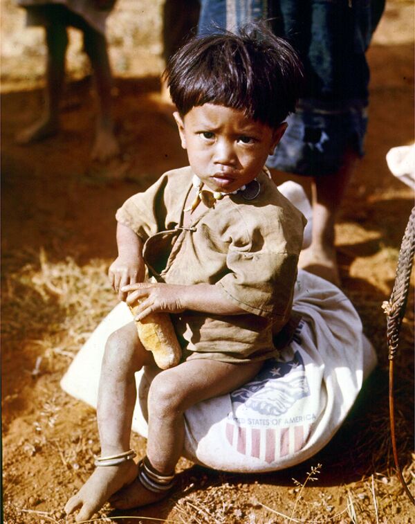 Вьетнамский маленький мальчик ест, сидя на мешке с американскими припасами, 1962 год. - Sputnik Беларусь