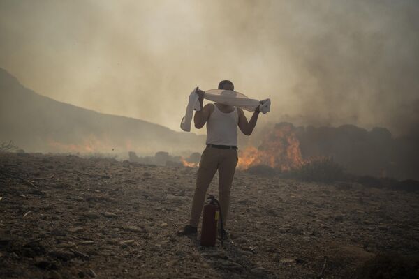 Мужчина прикрывает лицо полотенцем, пытаясь потушить пожар недалеко от морского курорта Линдос. - Sputnik Беларусь