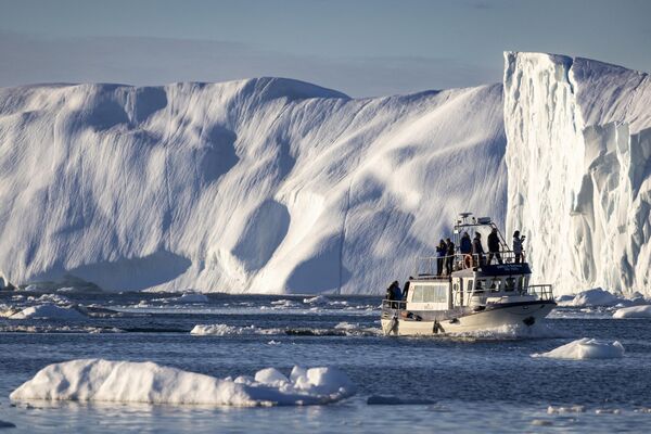 Лодка с туристами маневрирует среди айсбергов в заливе Диско в западной Гренландии. Массивные айсберги, отделяющиеся от ледника Якобсхавн в Северном полушарии, годами плавают в водах перед фьордом, а затем уносятся на юг океанскими течениями.  - Sputnik Беларусь