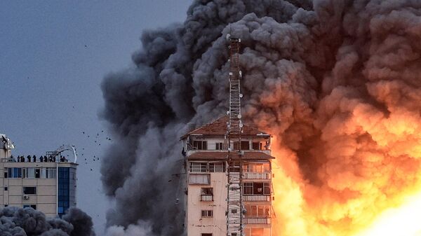 Люди, стоящие на крыше, наблюдают, как шар огня и дыма поднимается над зданием в городе Газа 7 октября 2023 года во время авиаудара Израиля по зданию Палестинской башни. - Sputnik Беларусь