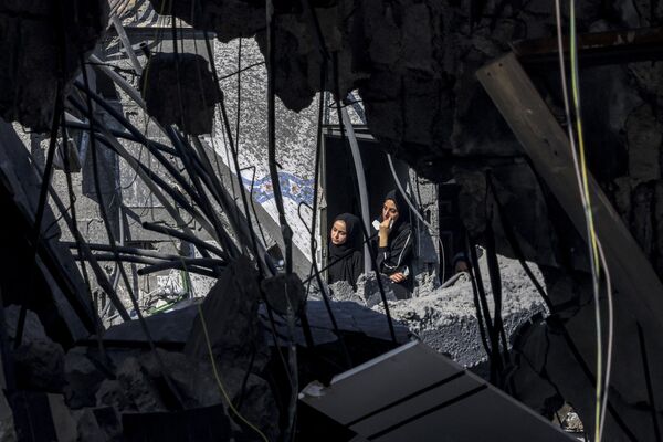 Население Газы после боев может не скоро вернуться к нормальной жизни, заявила бывшая советница палестинской переговорной группы по вопросам мира Хиба Хусейни.Как отметила бывшая советница, многие мирные палестинцы уже заявили, что скорее предпочтут умереть, нежели согласятся на эвакуацию и покинут родные дома, даже несмотря на продолжающееся кровопролитие. На фото: женщины выглядывают из окна здания, пострадавшего от израильской бомбардировки, в Рафахе на юге сектора Газа 31 октября 2023 года. - Sputnik Беларусь