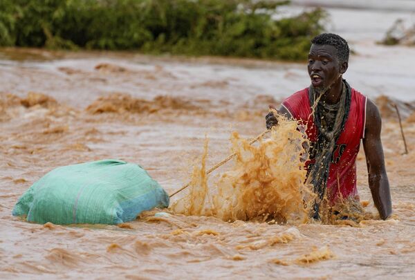Во второй половине октября в Кении начались сильные дожди, которые продолжаются до сих пор. Наводнения затронули как прибрежные районы на востоке страны, так и области на юго-востоке и севере. Отмечается, что наибольший урон нанесен прибрежному городу Момбаса, многие районы которого оказались под водой.По данным на 20 декабря, число погибших составило 174 человека, на территории страны установлены 170 лагерей для вынужденно перемещенных лиц, в них размещены более 545 тысяч человек.На фото: мужчина тянет свои вещи, пытаясь перейти дорогу, поврежденную дождями Эль-Ниньо, в Туле, округ Тана-Ривер в Кении, в субботу, 25 ноября 2023 года. - Sputnik Беларусь