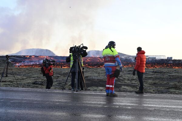 Представители СМИ и сотрудники службы экстренной помощи наблюдают, как поток лавы приближается к дороге на окраине юго-западного исландского города Гриндавик после извержения - Sputnik Беларусь