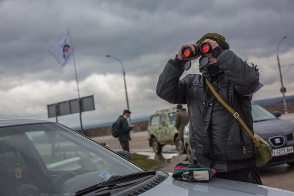 Местный житель наблюдает в бинокль за военным блокпостом на въезде в аэропорт &quot;Бельбек&quot; рядом с Севастополем. 28 февраля 2014 года. - Sputnik Беларусь