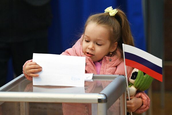 Девочка опускает в избирательную урну бюллетень на избирательном участке в посольстве РФ в Минске . - Sputnik Беларусь