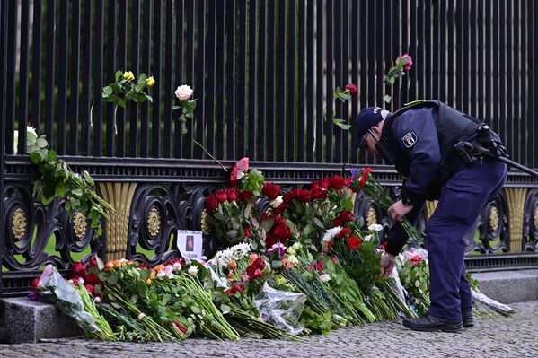 Сотрудник полиции — единственный человек, имеющий доступ к забору, — возлагает цветы возле посольства России в Берлине - Sputnik Беларусь