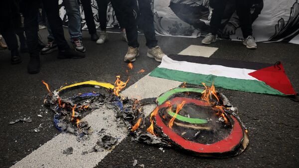 Протестующие сжигают олимпийские кольца на тротуаре возле палестинского флага во время первомайской демонстрации в среду, 1 мая 2024 года, в Париже - Sputnik Беларусь