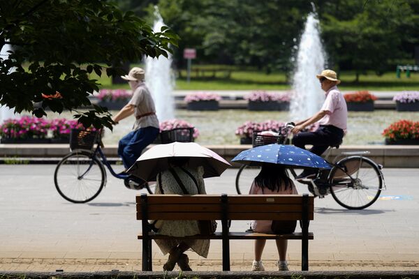 Людзі з парасонамі сядзяць на лаўцы пад пякучым сонцам у парку Токіа, Японія. - Sputnik Беларусь