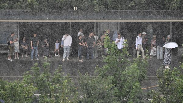 Люди на остановке общественного транспорта во время ливня - Sputnik Беларусь
