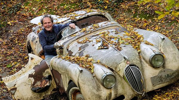 Коллекционер автомобилей Михаэль Фрёлих на фоне старинного автомобиля Jaguar XK120 в своем частном парке в Меттманне, Германия - Sputnik Беларусь