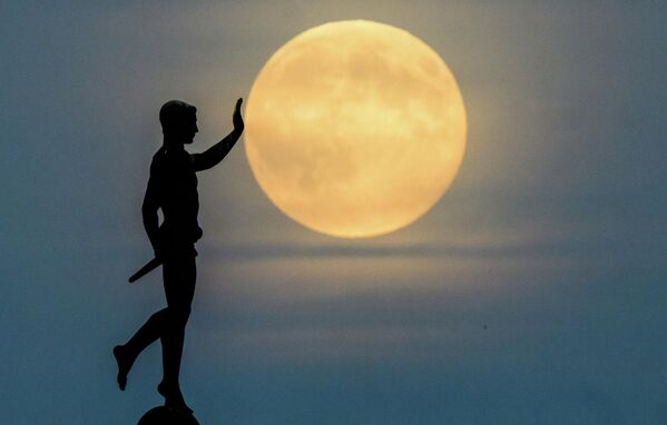 Луна восходит на горизонте за статуей "Факелоносец" на северном берегу озера Маш, Германия.