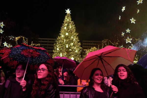 Публика слушает концерт под дождем в центре Афин на фоне сияющей рождественской елки. - Sputnik Беларусь