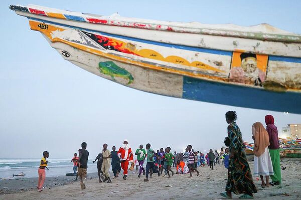 Санта-Клаус раздает подарки и сладости детям на пляже в бедном районе города Дакар в Сенегале.
