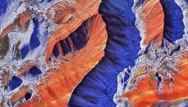 Вид с воздуха на живописный район Цицай Данся (или знаменитые Радужные горы) под падающим снегом в геопарке Чжанъе, провинция Ганьсу, Китай.