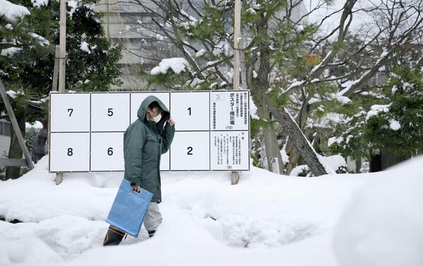На фотографии, сделанной агентством Kyodo, житель города Фукуи в Японии пробирается через сугробы мимо доски объявлений с плакатами кандидатов на внеочередных выборах. - Sputnik Беларусь