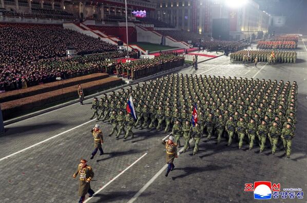 Военнослужащие, принимавшие участие в освобождении и разминировании Курской области, идут строем с флагами России и КНДР.