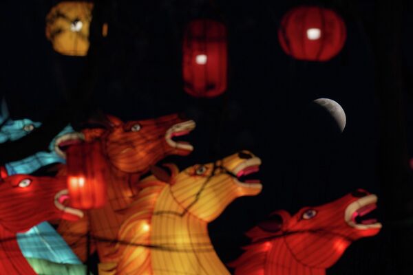 Луна незадолго до полного затмения на фоне фонарей в форме лошадиных голов в Пекине.