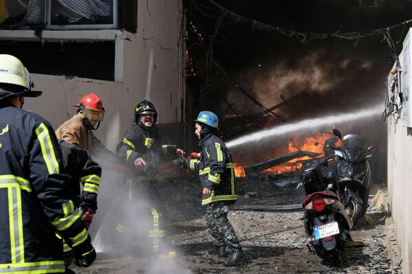 Пожарные пытаются потушить пламя на месте израильского авиаудара по многоквартирному дому в Бейруте.