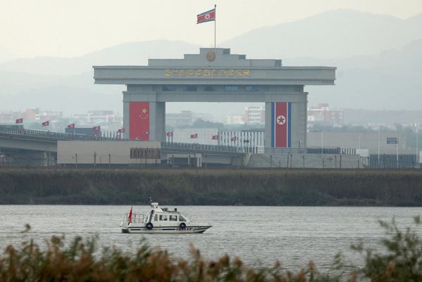 Китайское судно иммиграционной службы движется по реке Ялуцзян мимо здания северокорейской таможни. - Sputnik Беларусь