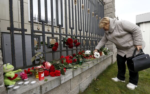 Женщина возлагает цветы к ограде посольства РФ в Минске - Sputnik Беларусь