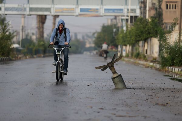 Велосипедист проезжает мимо оболочки бомбы в Думе, Дамаск, Сирия - Sputnik Беларусь