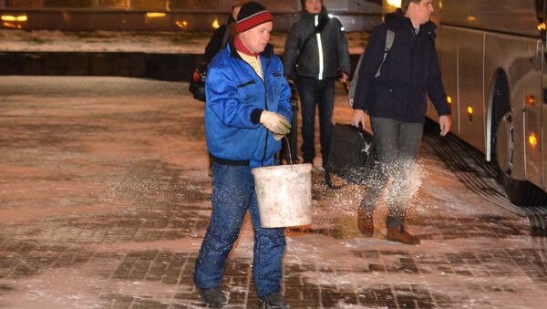 Работник ЖКХ посыпает солью скользкую плитку возле гостиницы Планета - Sputnik Беларусь