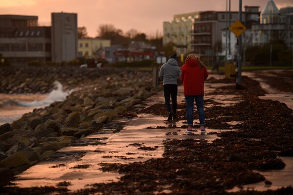 Люди ходят по дороге, покрытой водорослями, после шторма Офелия в Ирландии - Sputnik Беларусь
