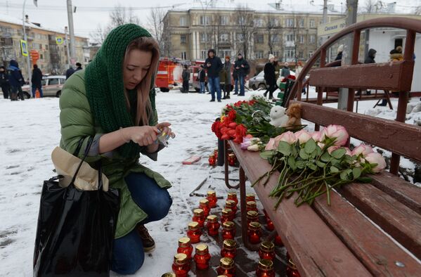 Женщина зажигает свечу возле здания торгового центра Зимняя вишня в Кемерово, где произошел пожар. - Sputnik Беларусь
