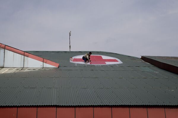 Рабочий рисует эмблему медицинского креста на крыше госпиталя SMHS в Сринагаре во время эскалации напряженности между Индией и Пакистаном  - Sputnik Беларусь