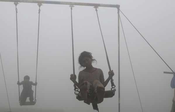 Дети катаются на качелях на детской площадке, окруженной смогом, в Лахоре - Sputnik Беларусь