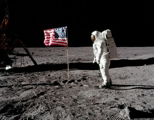 Астронавт Базз Олдрин, пилот лунного модуля, возле развернутого флага США во время выхода на Луну 20 июля 1969 года. Лунный модуль находится слева, на поверхности видны следы космонавтов. Фото Нила Армстронга.  - Sputnik Беларусь