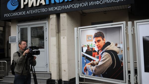 Видеооператор у фотографии погибшего на Украине фотокорреспондента Андрея Стенина у здания МИА Россия сегодня - Sputnik Беларусь