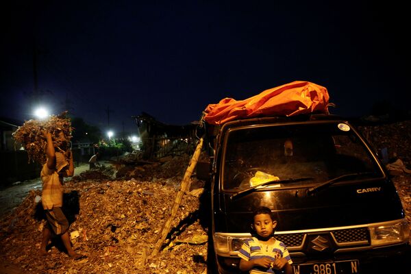 Ребенок ждет, пока взрослые занимаются погрузкой мусора в деревне Бангун в Индонезии - Sputnik Беларусь